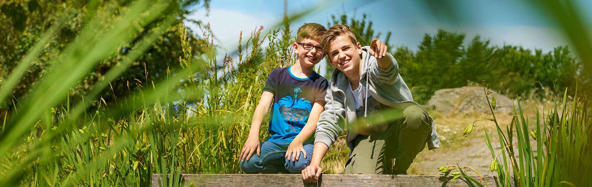 Zwei Jungs sitzen auf Holzbrücke und schauen ins Grüne