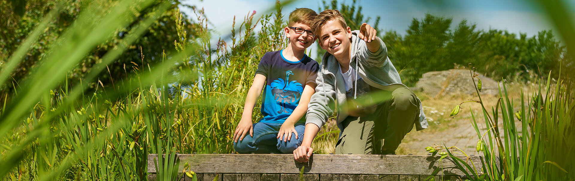 Zwei Jungs sitzen auf Holzbrücke und schauen ins Grüne